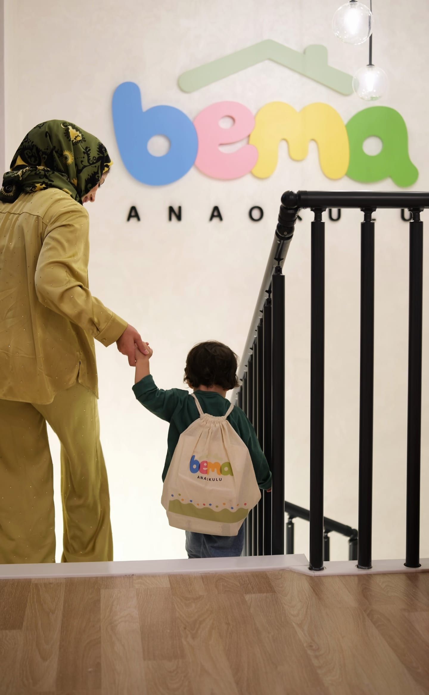 BEMA Anaokulu logolu duvarın önünde merdivenden inen veli ve çocuk